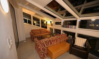 A cozy room with large windows and modern furnishings. The furniture consists of a red sofa, an armchair, and a wooden table.