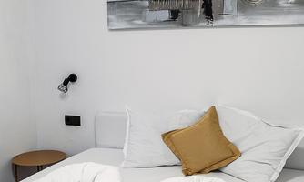 A modern bedroom with a large bed and artistic wall decoration. The pillows are in warm shades of yellow.