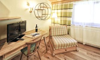 A cozy room with a television, a desk, and a comfortable armchair. The light is warm, and the space has an inviting atmosphere.