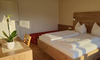 A bright and modern bedroom with a large double bed and a red couch. A plant sits on the table and the light streams softly through the window.
