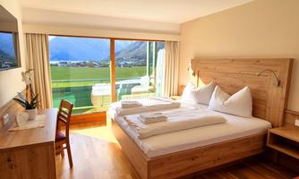 A cozy hotel room with a double bed and a view of the mountains. The large window front lets in plenty of daylight.