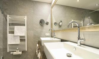 A modern bathroom with a sink and a large mirror. A towel rack hangs on the wall and the walls are gray tiles.