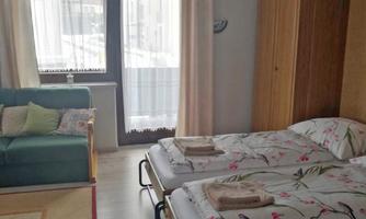 A cozy bedroom with two single beds and a green sofa. Large windows let in plenty of light, and the room feels bright and inviting.