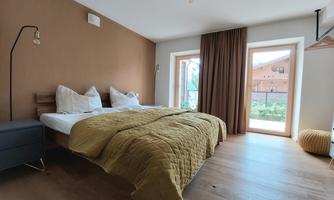 A bright bedroom with a cozy double bed and neatly folded blankets. Large windows provide a view of the outdoors.