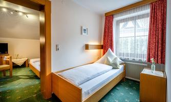 A bright room with two beds and a large window. The walls are painted in neutral colors, and there is a cozy seating area.