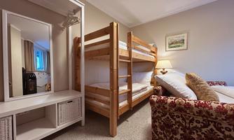 A cozy room with a wooden bunk bed and a sofa. A large mirror and a lamp create a bright atmosphere.