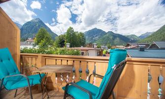 A cozy balcony with two chairs and a table. In the background, impressive mountains and a clear sky can be seen.