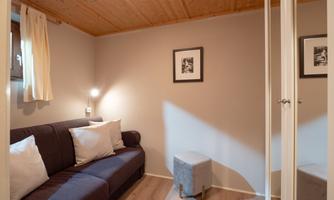 A cozy room with a sofa and two cushions. Pictures hang on the wall and there is a mirror.