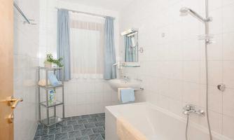 A modern bathroom with a bathtub and a shower. The walls are tiled, and there are curtains in gentle colors.