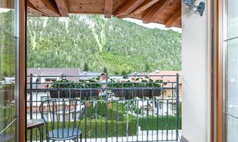A balcony overlooking green mountains and cozy houses. A atmospheric ambiance with plants and wooden paneling.