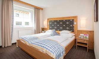A cozy bedroom with a large double bed and light curtains. The walls are made of wood, and the room is designed in a clear and inviting manner.