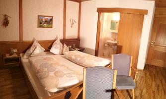 A cozy bedroom with a double bed and two pillows. There is a chair and a view of a bathroom with wooden details.