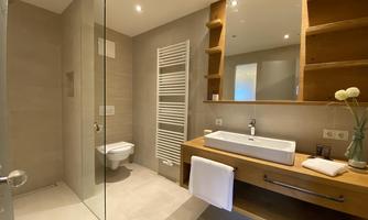 A modern bathroom with a glass shower cubicle and a wooden vanity. The lighting is bright and welcoming, and the decor is simple and elegant.