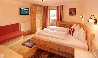 A cozy bedroom with a large bed and a sitting area. The wooden furniture gives the room a warm atmosphere.