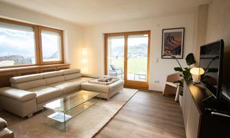 A modern living room with a large, comfortable sofa and glass table. Large windows provide a beautiful view of the nature outside.