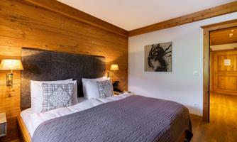 A cozy bedroom with a large bed and wooden walls. The soft lighting creates an inviting atmosphere.