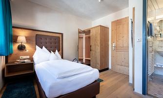 A modern hotel room with a comfortable bed and wooden cabinets. The room is bright and friendly, with a window that leads to the bathroom.
