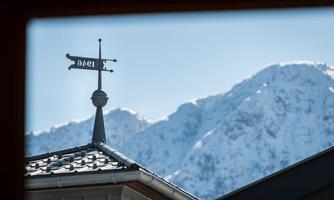 A roof with a ptarmigan and a peak in the background. The mountains are covered in snow and the sky is clear.
