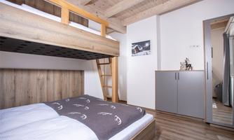 A cozy bedroom with a bunk bed and modern furniture. The wooden ceiling gives the room a warm atmosphere.