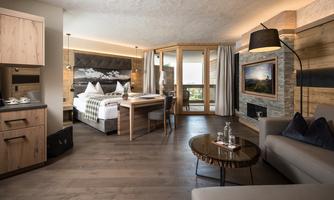 A modern room with wooden decor and large windows. There is a cozy bed, a table, and a seating area.