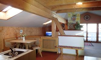 A cozy apartment with wooden beams and open space. There is a dining area and a television, as well as large windows for plenty of light.