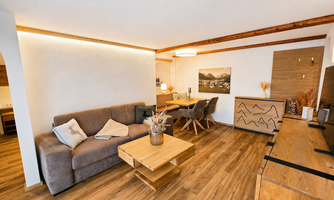 A modern living room with a gray sofa and a wooden table. Pictures hang on the wall and the atmosphere is cozy and bright.