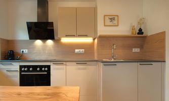 A modern kitchen with elegant wooden and white furniture. The refrigerator, stove, and sink are well arranged, and the lighting creates a pleasant atmosphere.