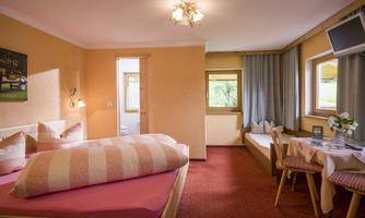 A cozy room with a double bed and an additional sleeping space. Bright walls and a window that overlooks a green view.