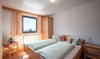 An inviting bedroom with a large bed and green and white checked bedspreads. Natural light shines through the window, creating a bright, cozy atmosphere.
