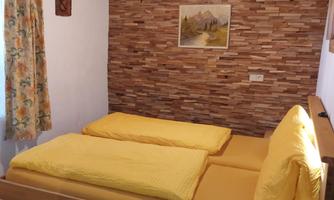 A cozy bedroom with two single beds and yellow bedspreads. The walls are covered with wood, and a large window lets in plenty of light.