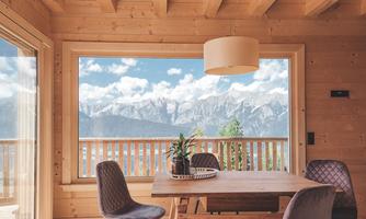 A bright and modern dining room with wooden cladding. Through the large window, there is a view of the majestic mountains and the blue sky.