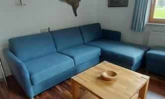 A cozy living room with a blue sofa and a wooden table. The walls are light, and the window offers a view outside.