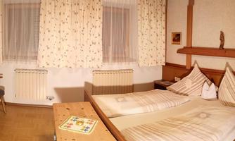 A cozy hotel room with two single beds, a television, and a small table. The walls are adorned with floral patterns and there are large windows with curtains.
