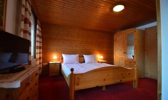 A cozy bedroom with two beds and wooden paneling. There is soft lighting and a television in the room.