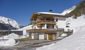 A modern house in the mountains, surrounded by snow and mountain landscapes. The clear blue sky completes the winter scene.