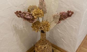 A decorative vase with dried flowers is in a corner. The floor is made of wood and the wall has a light color.