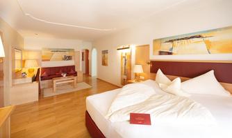 A modern hotel room with a large bed and a cozy seating area. Bright walls and warm wood create an inviting atmosphere.