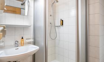 A modern bathroom with a glass-layered shower and a sink. The walls are tiled and a wooden ceiling creates a cozy atmosphere.