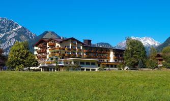 A beautiful hotel with balconies amidst green meadows. In the background, majestic mountains and a clear blue sky can be seen.