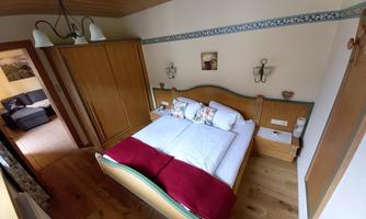 A cozy bedroom with a double bed and a red throw. In the background, there are wooden wardrobes and a pleasant living atmosphere.