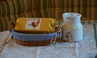 A basket with fresh eggs and a metallic milk can on a table. The tablecloth is designed with a simple pattern.