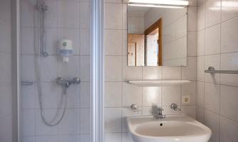 A modern bathroom with a shower cubicle and a sink. The wall is tiled in neutral colors.