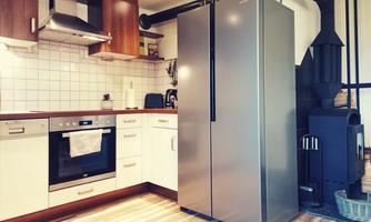 A modern kitchen with wood and stainless steel elements. The refrigerator stands next to an oven and a fireplace.