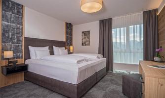 A modernly furnished bedroom with a large double bed and bright curtains. The room features cozy furniture and a view of the outdoor landscape.