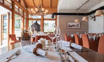An elegant restaurant with stylish table settings and inviting chairs. Large windows let in plenty of daylight and offer a view of the surroundings.