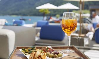 A beautiful table with a plate of delicious snacks and a drink outdoors. In the background, you can see a picturesque lake and mountains.