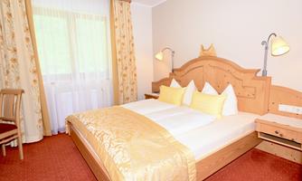 A cozy bedroom with a large double bed and warm colors. The light curtains and wooden decor create an inviting atmosphere.