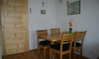 A cozy dining area with a wooden table and four chairs. Pictures hang on the wall and a wooden board serves as a door.