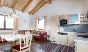 A bright and modern kitchen with an open living area. The space features high wooden beams and a cozy seating area.