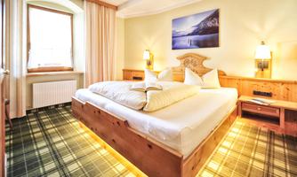 A cozy bedroom with a large wooden bed and a softly padded headboard. The walls are light, and a picture of a mountain landscape hangs above it.